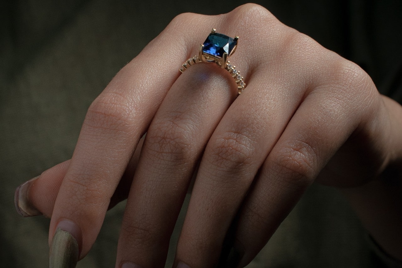 lady’s hand wearing a fashion ring with a blue gemstone and diamonds