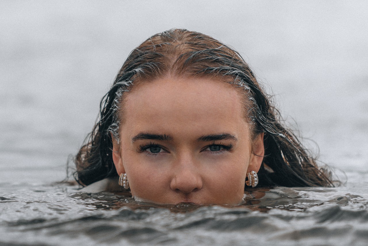 A woman whose face is half-submerged in water is wearing pearl huggies earrings A woman whose face is half-submerged in water is wearing pearl huggies earrings