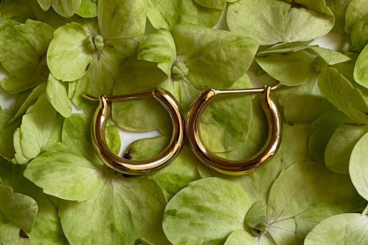 A pair of yellow gold huggies earrings on a bed of green leaves A pair of yellow gold huggies earrings on a bed of green leaves