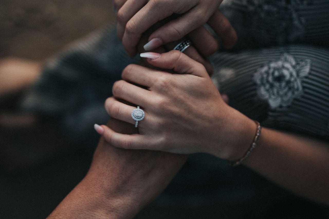 A couple holding hands, the woman wearing a halo engagement ring A couple holding hands, the woman wearing a halo engagement ring