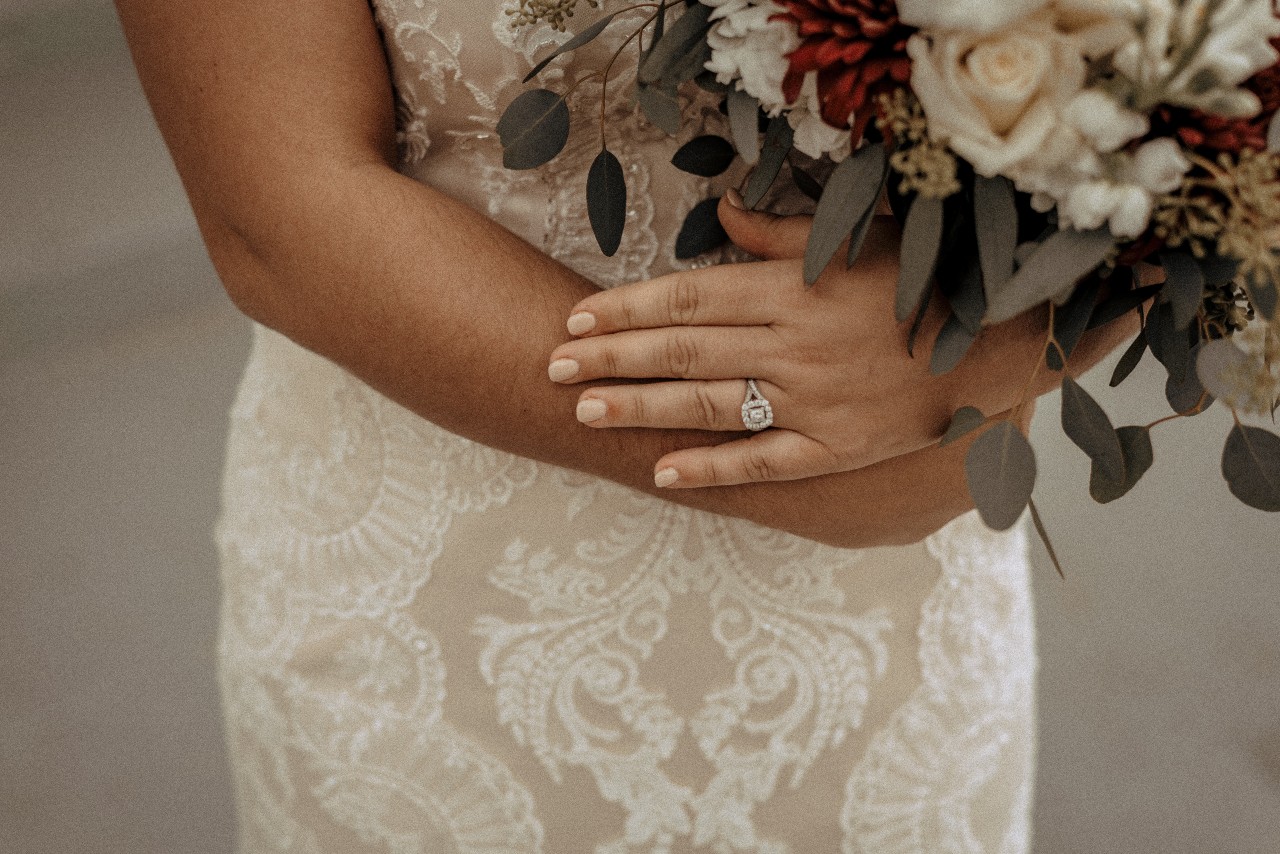A bride holds her bouquet of flowers while wearing her princess-cut halo engagement ring A bride holds her bouquet of flowers while wearing her princess-cut halo engagement ring