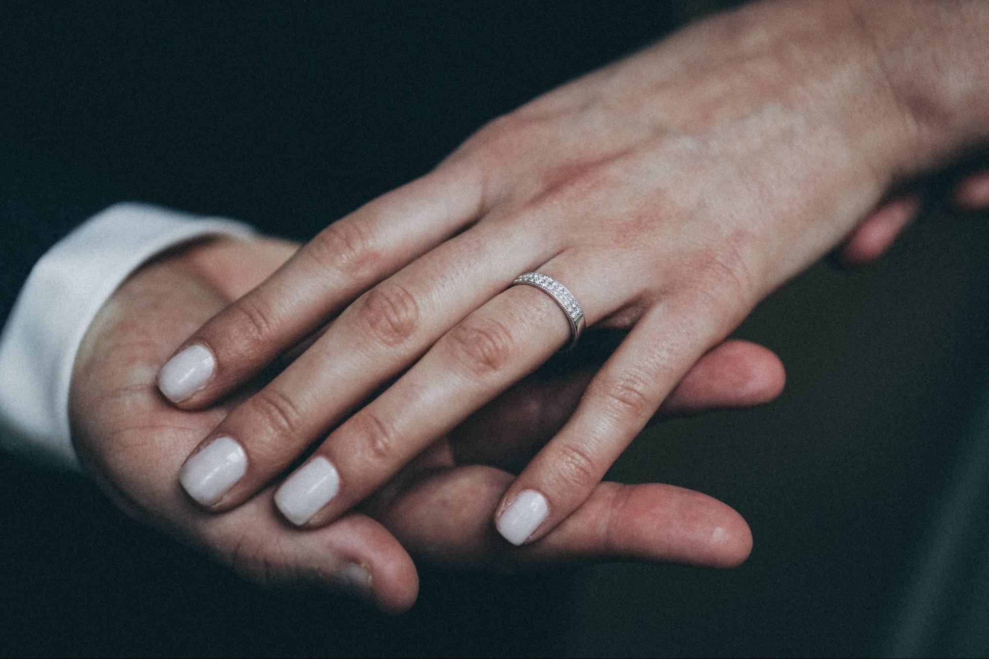 A woman rests her hand on her husband's to show off her diamond wedding band A woman rests her hand on her husband's to show off her diamond wedding band