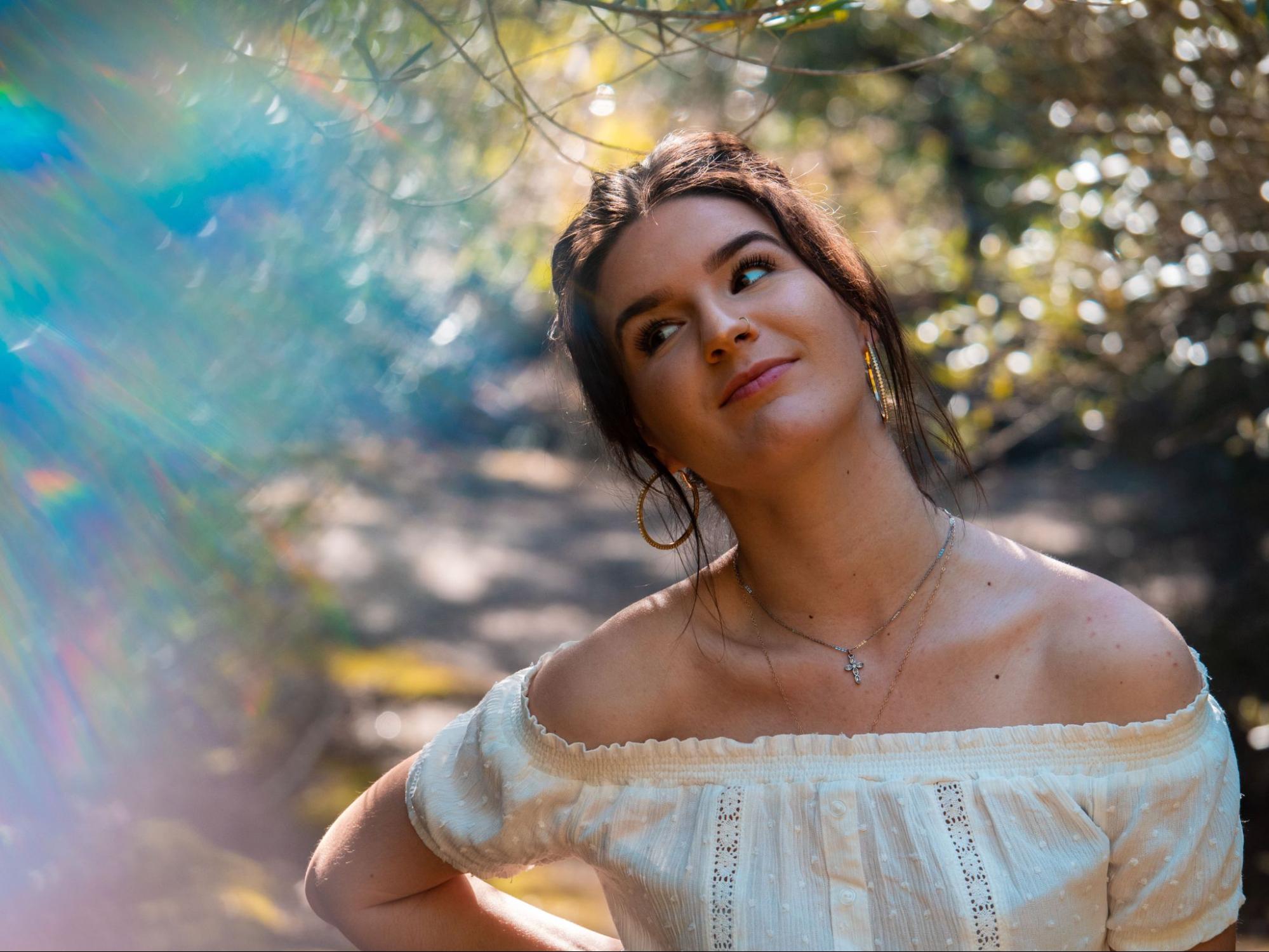 Young woman in an off-the-shoulder white blouse looks upward with a thoughtful expression, showcasing a silver cross necklace. Young woman in an off-the-shoulder white blouse looks upward with a thoughtful expression, showcasing a silver cross necklace.