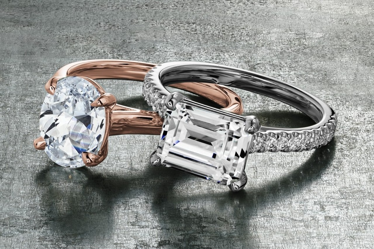 A rose gold, oval cut engagement ring next to a silver, emerald cut engagement ring A rose gold, oval cut engagement ring next to a silver, emerald cut engagement ring