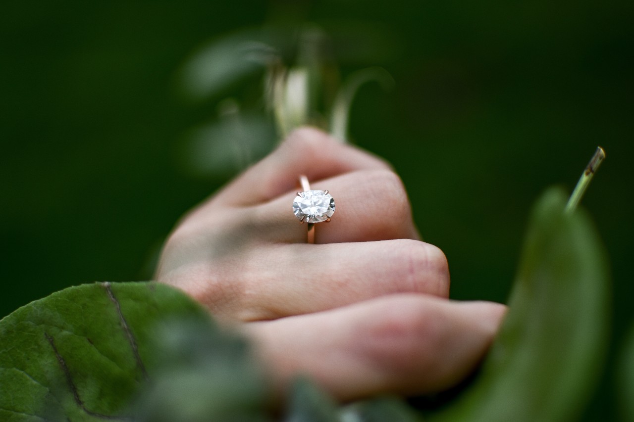 An oval cut diamond solitaire engagement ring on a woman's finger as she grabs a plant An oval cut diamond solitaire engagement ring on a woman's finger as she grabs a plant