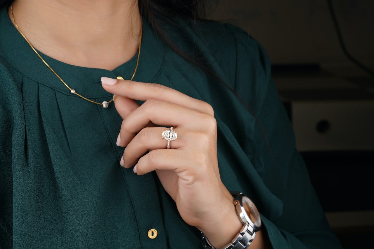 A woman wearing an oval cut engagement ring touches a necklace on her blouse A woman wearing an oval cut engagement ring touches a necklace on her blouse