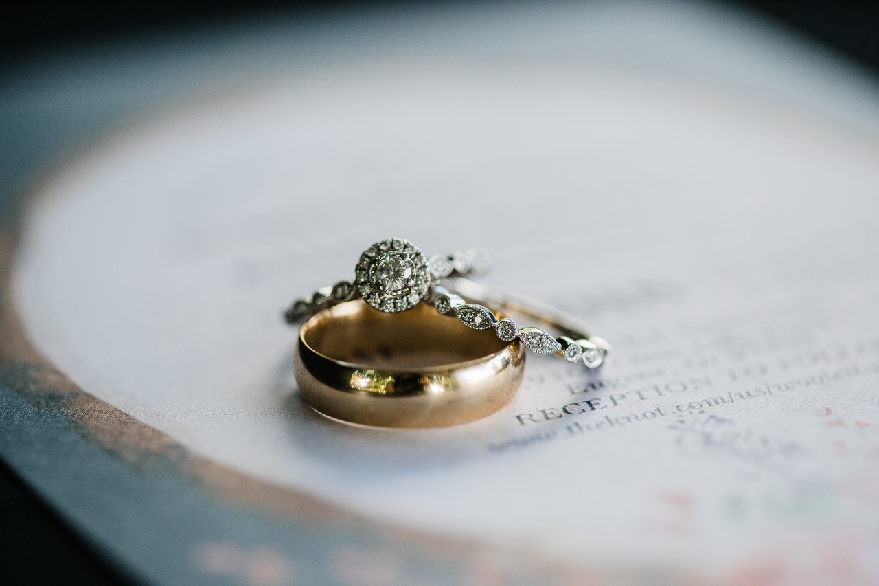 A vintage halo engagement ring with a matching band and gold band sitting on a wedding invitation A vintage halo engagement ring with a matching band and gold band sitting on a wedding invitation