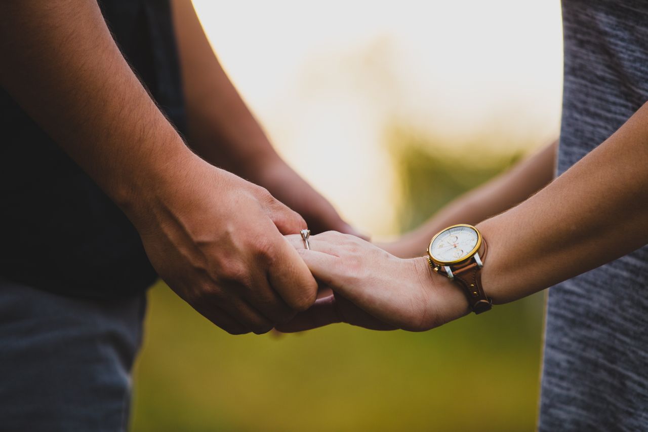 A couple holding hands, woman wears a solitaire engagement ring A couple holding hands, woman wears a solitaire engagement ring