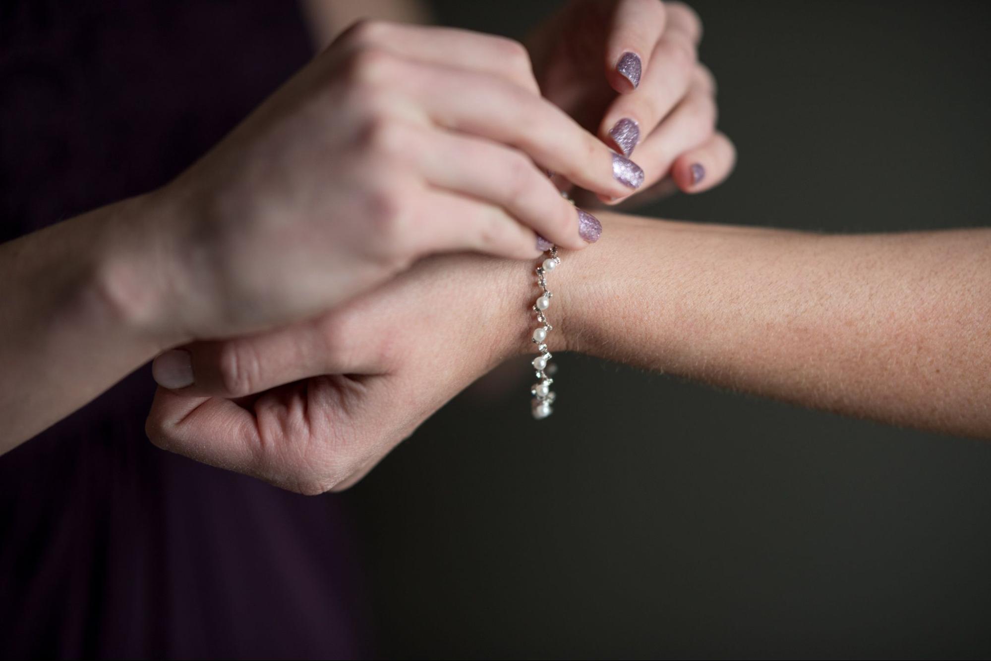 A person is fastening a delicate pearl and crystal bracelet onto another person’s wrist, both with well-manicured hands. A person is fastening a delicate pearl and crystal bracelet onto another person’s wrist, both with well-manicured hands.