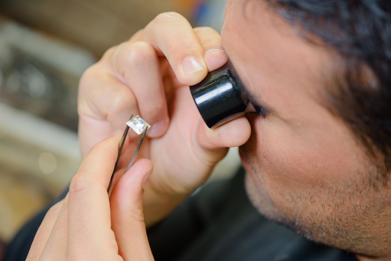 An expert gemologist inspects a princess-cut lab-grown diamond for perfection before placing it in a ring setting An expert gemologist inspects a princess-cut lab-grown diamond for perfection before placing it in a ring setting