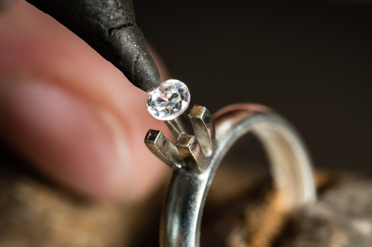 A professional gemologist carefully places a lab-grown round-cut diamond into the prongs of a platinum solitaire engagement ring A professional gemologist carefully places a lab-grown round-cut diamond into the prongs of a platinum solitaire engagement ring
