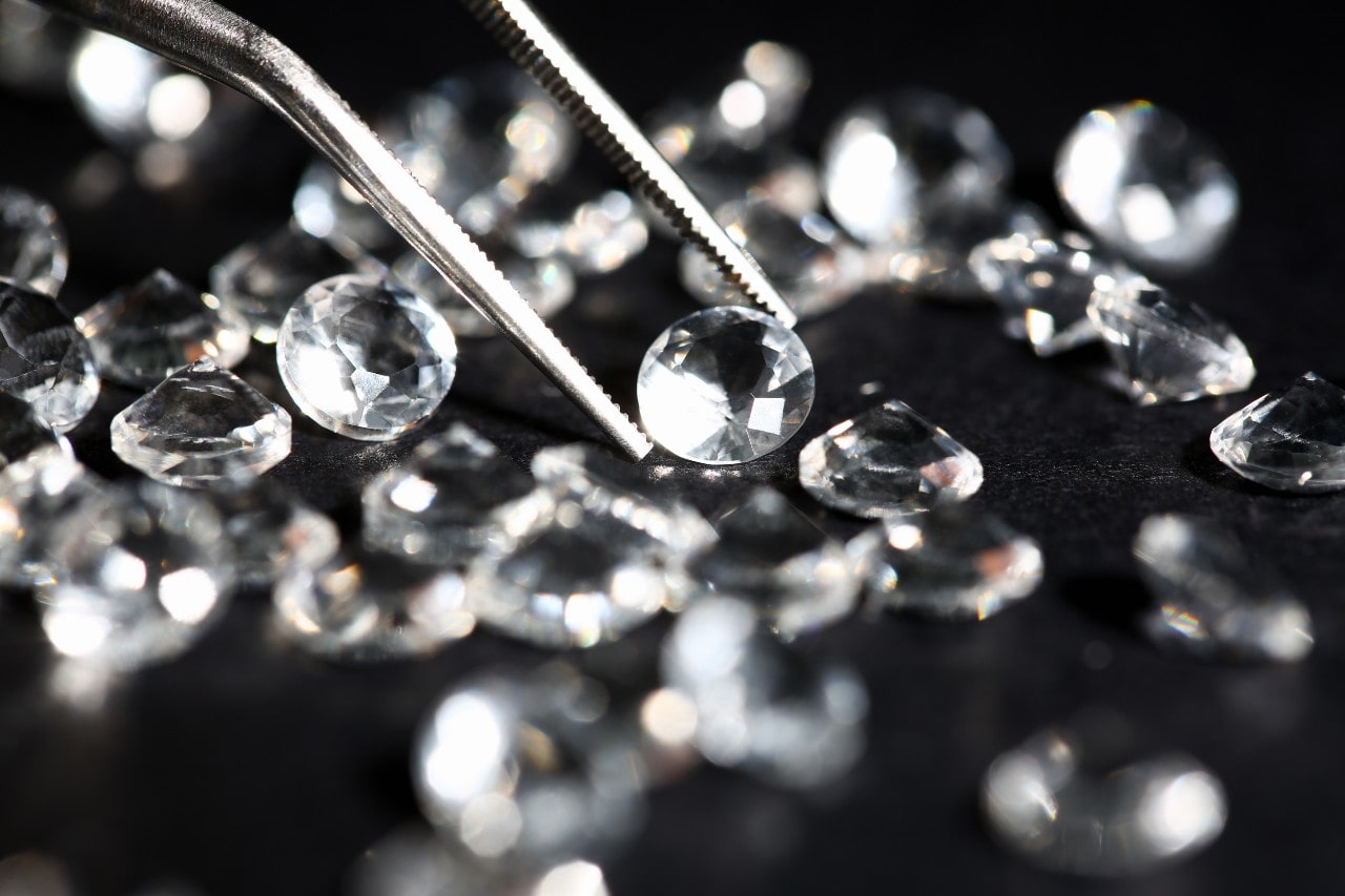 A close-up of a jeweler selecting a round-cut diamond with a pair of jewelry tweezers.