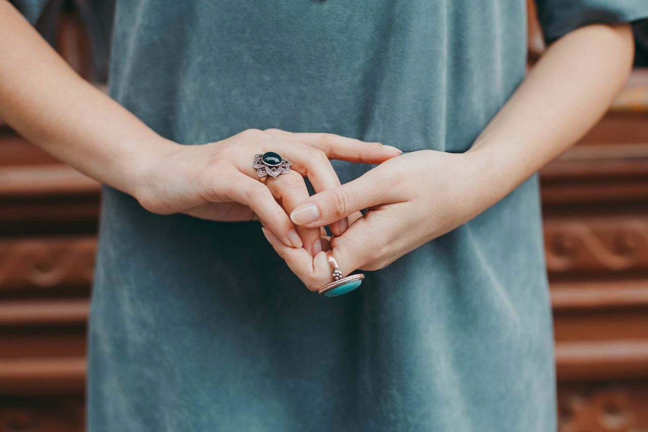 A close-up of a woman’s clasped hands, wearing two bold and fashionable rings.