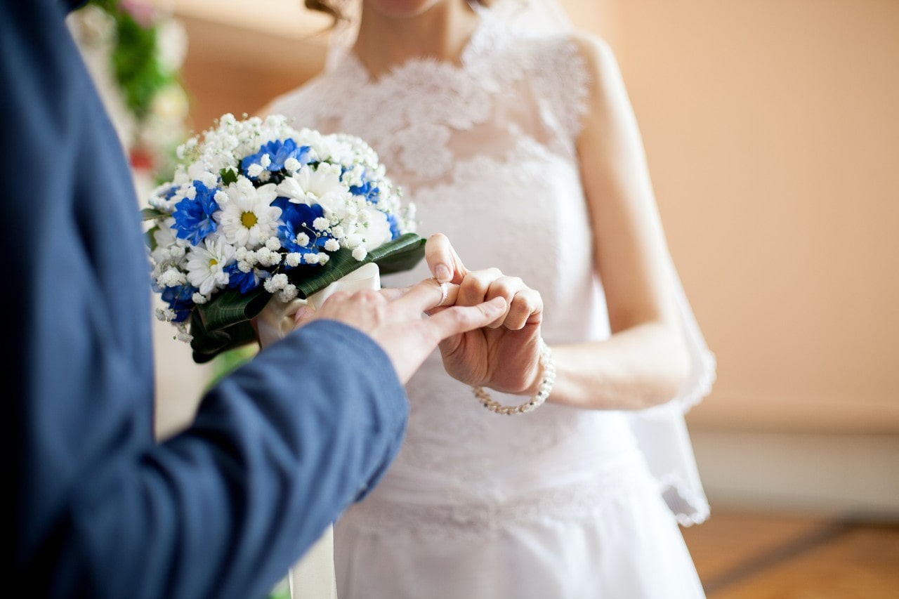 a bride and groom holding flowers and putting on their wedding bands