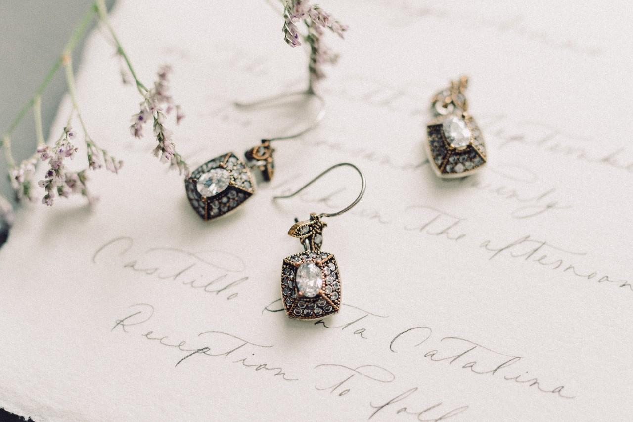 A close-up of two pairs of stunning diamond earrings displayed atop a written wedding invitation.