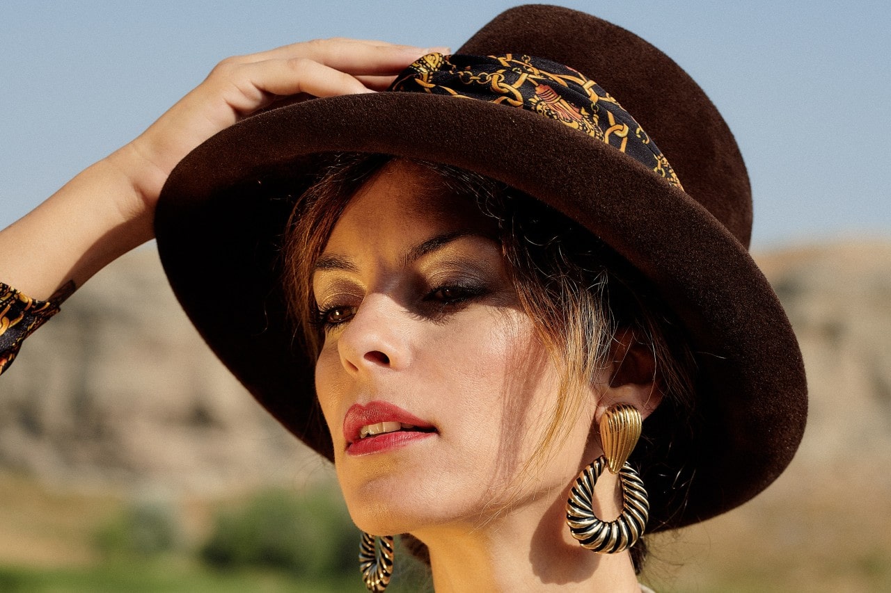 A close-up of a fashionably dressed woman, wearing bold earrings and an elegant hat.