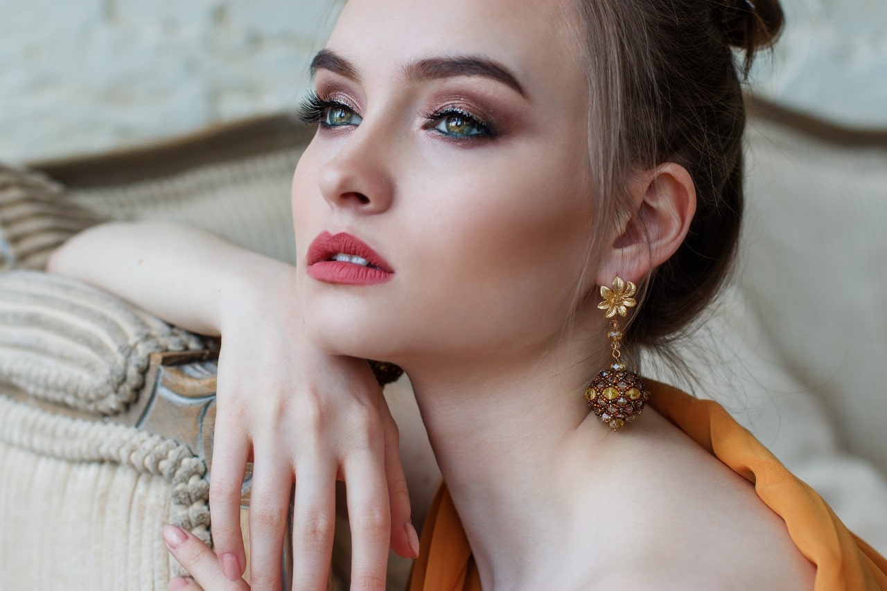 A young woman lounging on a sofa, wearing distinctive earrings.