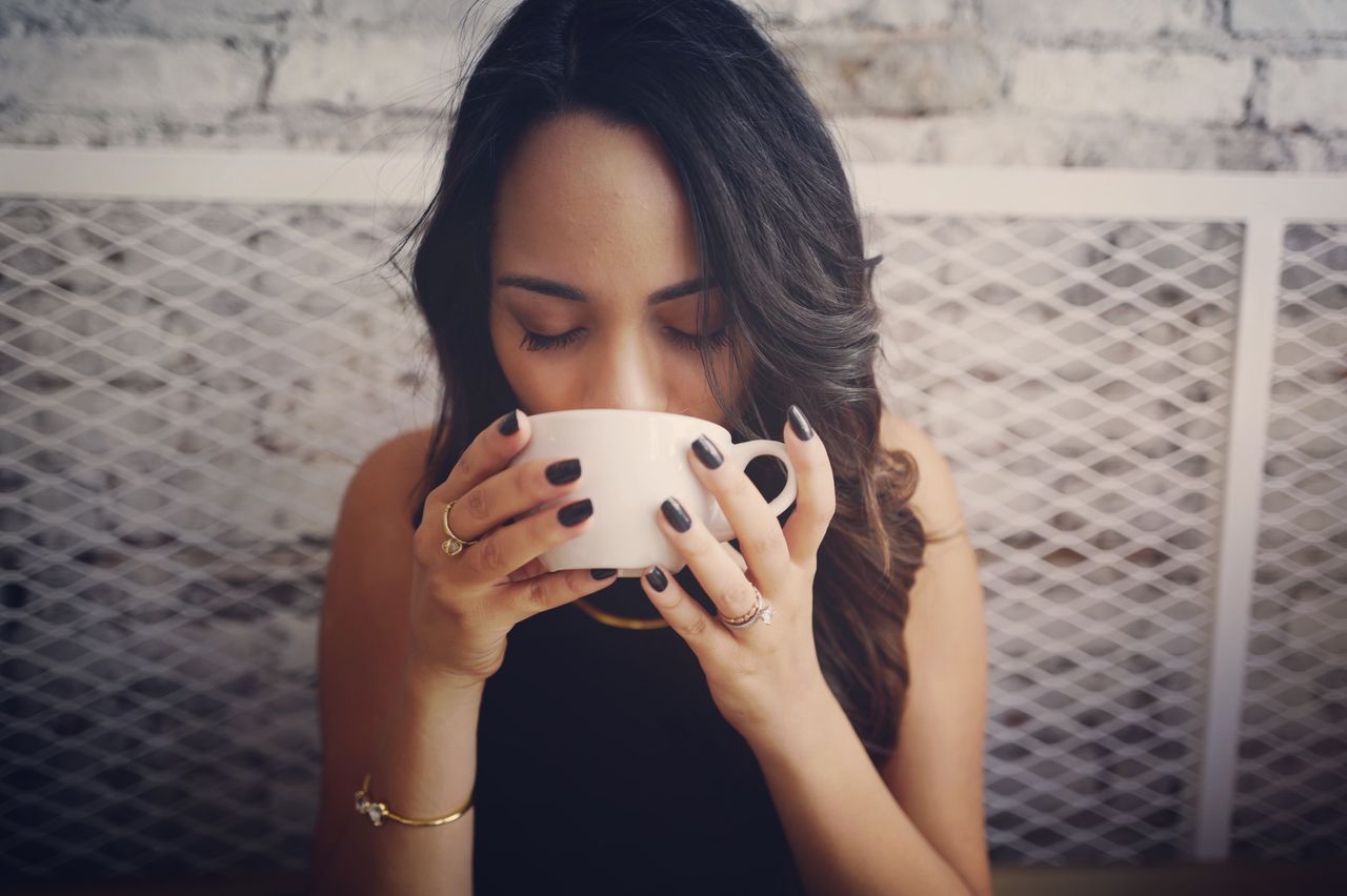 An elegant young woman sipping coffee, wearing minimalist fashion jewellery.