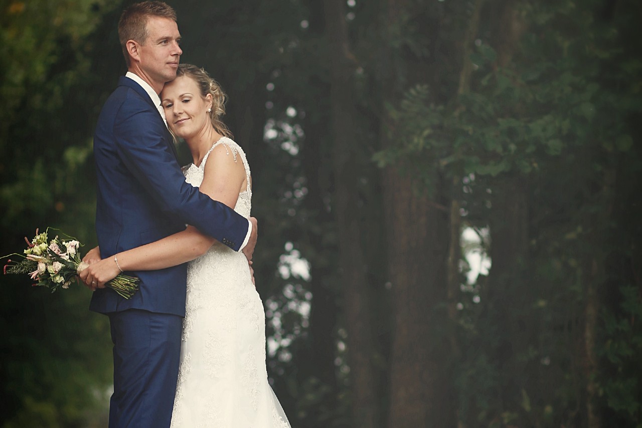 A bride and groom embracing in a wooded area.