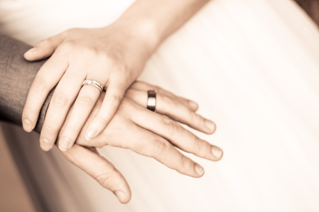two hands clasped and wearing wedding bands