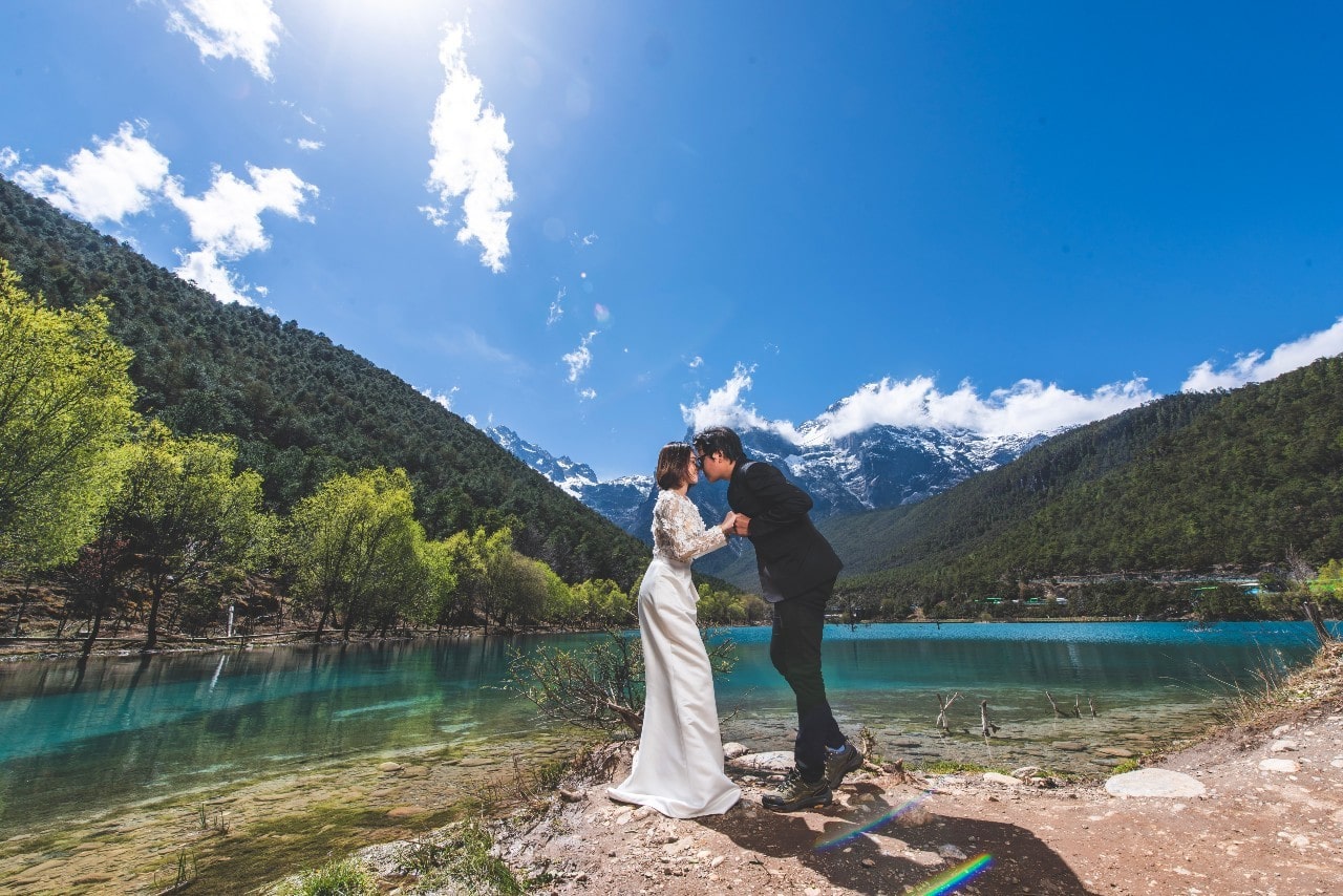 A bride and groom sharing a kiss in front of a scenic lakeside.