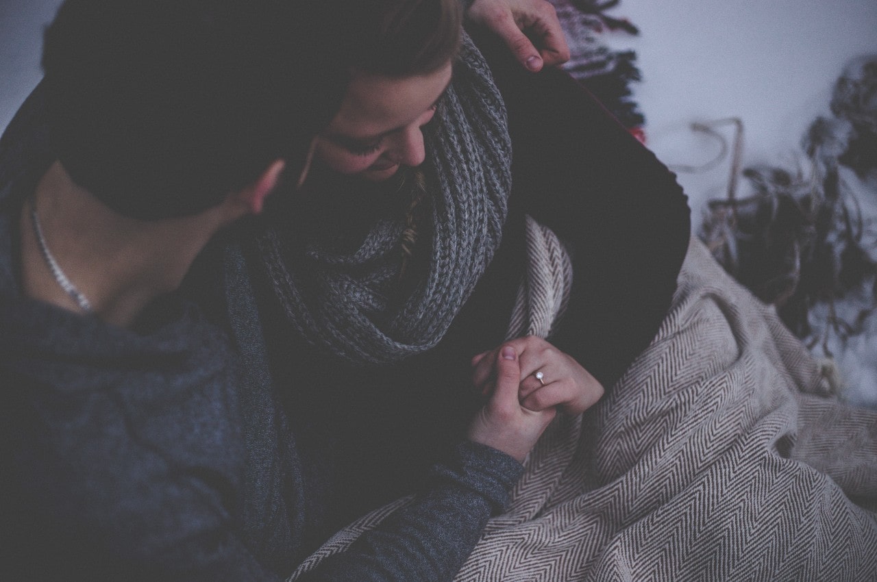 A cozy couple bundled up on a cold day, with focus on the bride-to-be’s engagement ring.