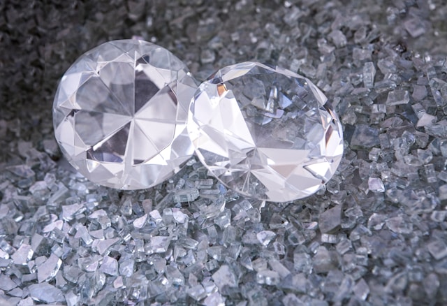 A close-up of two round cut diamonds displayed atop diamond cuttings.