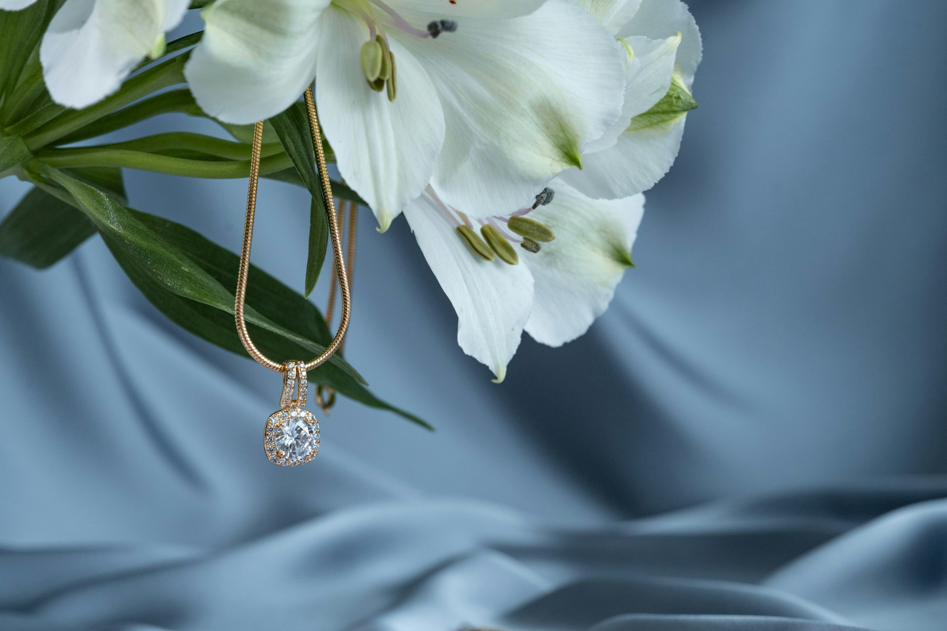 A yellow gold diamond pendant necklace hanging from a bouquet of white flowers.