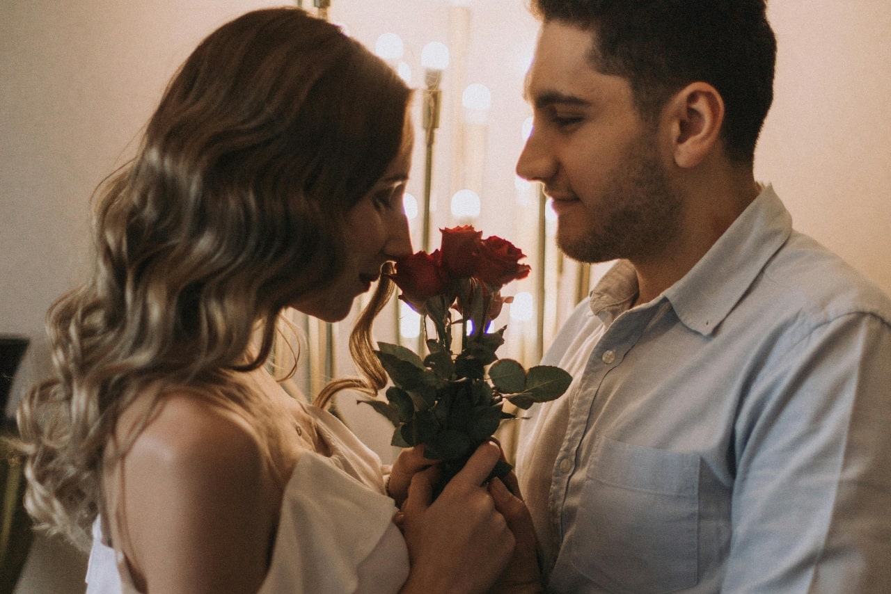 A woman smelling the roses that her boyfriend is holding to give her for Valentine’s Day